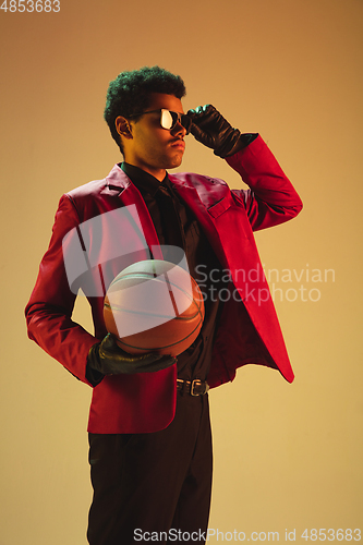 Image of High-fashion styled man in red jacket playing basketball isolted over brown background