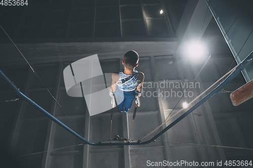 Image of Little male gymnast training in gym, flexible and active. Caucasian fit little boy, athlete in sportswear practicing in exercises for strength, balance.