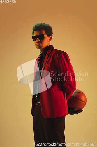 Image of High-fashion styled man in red jacket playing basketball isolted over brown background