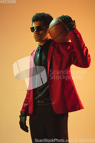 Image of High-fashion styled man in red jacket playing basketball isolted over brown background