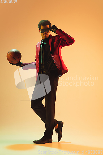 Image of High-fashion styled man in red jacket playing basketball isolted over brown background