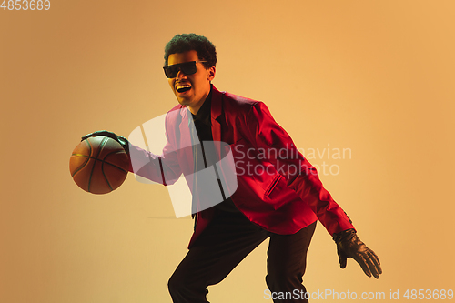 Image of High-fashion styled man in red jacket playing basketball isolted over brown background