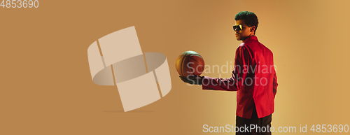 Image of High-fashion styled man in red jacket playing basketball isolted over brown background