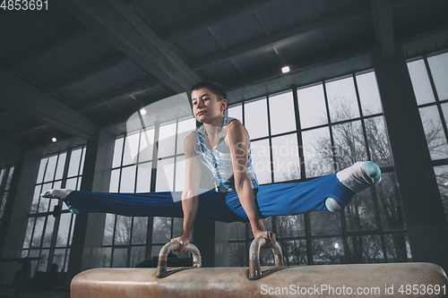 Image of Little male gymnast training in gym, flexible and active. Caucasian fit little boy, athlete in sportswear practicing in exercises for strength, balance.