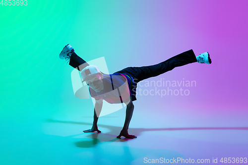 Image of Beautiful sportive boy dancing hip-hop in stylish clothes on colorful gradient background at dance hall in neon light.