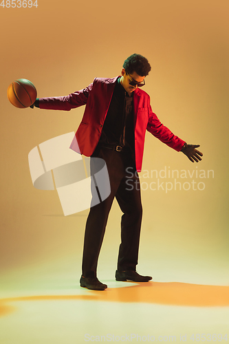 Image of High-fashion styled man in red jacket playing basketball isolted over brown background