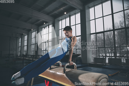 Image of Little male gymnast training in gym, flexible and active. Caucasian fit little boy, athlete in sportswear practicing in exercises for strength, balance.