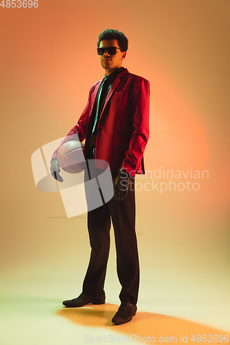 Image of High-fashion styled man in red jacket playing basketball isolted over brown background