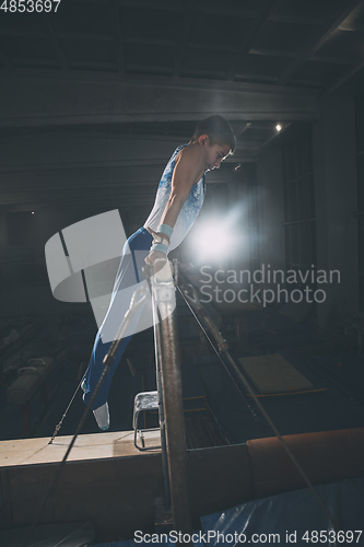 Image of Little male gymnast training in gym, flexible and active. Caucasian fit little boy, athlete in sportswear practicing in exercises for strength, balance.