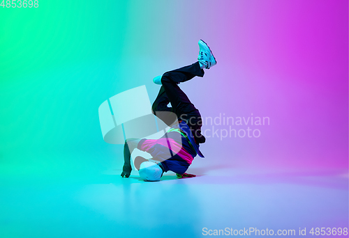 Image of Beautiful sportive boy dancing hip-hop in stylish clothes on colorful gradient background at dance hall in neon light.