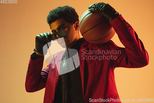 Image of High-fashion styled man in red jacket playing basketball isolted over brown background