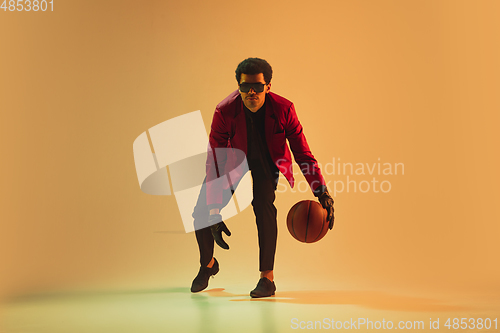 Image of High-fashion styled man in red jacket playing basketball isolted over brown background