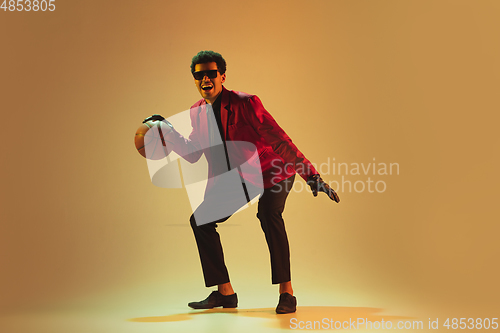 Image of High-fashion styled man in red jacket playing basketball isolted over brown background