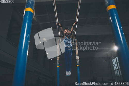 Image of Little male gymnast training in gym, flexible and active. Caucasian fit little boy, athlete in sportswear practicing in exercises for strength, balance.