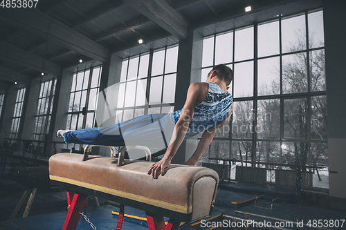 Image of Little male gymnast training in gym, flexible and active. Caucasian fit little boy, athlete in sportswear practicing in exercises for strength, balance.