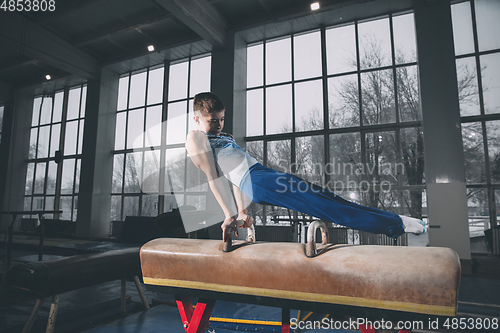 Image of Little male gymnast training in gym, flexible and active. Caucasian fit little boy, athlete in sportswear practicing in exercises for strength, balance.