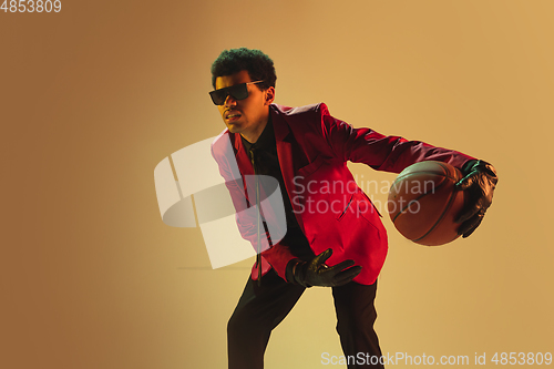 Image of High-fashion styled man in red jacket playing basketball isolted over brown background