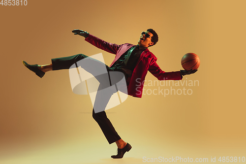 Image of High-fashion styled man in red jacket playing basketball isolted over brown background