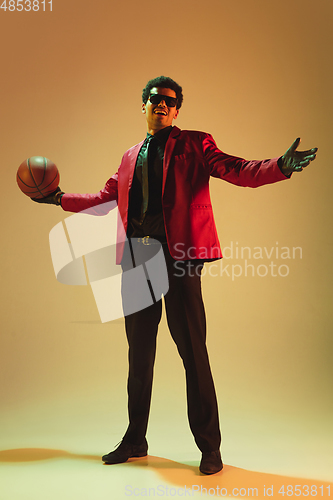 Image of High-fashion styled man in red jacket playing basketball isolted over brown background