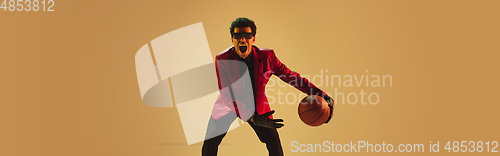 Image of High-fashion styled man in red jacket playing basketball isolted over brown background