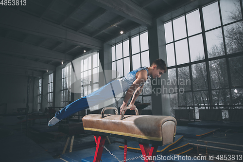 Image of Little male gymnast training in gym, flexible and active. Caucasian fit little boy, athlete in sportswear practicing in exercises for strength, balance.