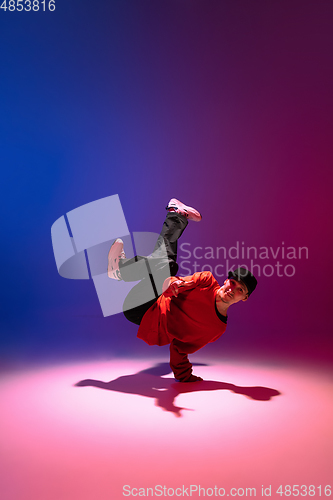 Image of Beautiful sportive boy dancing hip-hop in stylish clothes on colorful gradient background at dance hall in neon light.