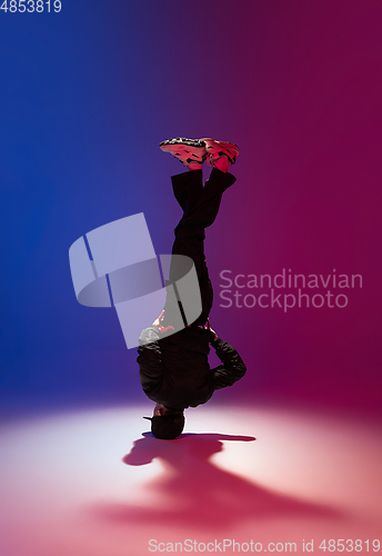 Image of Beautiful sportive boy dancing hip-hop in stylish clothes on colorful gradient background at dance hall in neon light.