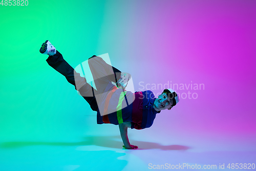 Image of Beautiful sportive boy dancing hip-hop in stylish clothes on colorful gradient background at dance hall in neon light.