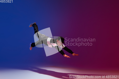 Image of Beautiful sportive boy dancing hip-hop in stylish clothes on colorful gradient background at dance hall in neon light.