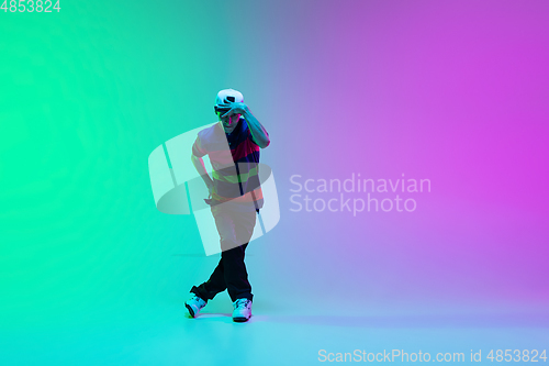 Image of Beautiful sportive boy dancing hip-hop in stylish clothes on colorful gradient background at dance hall in neon light.