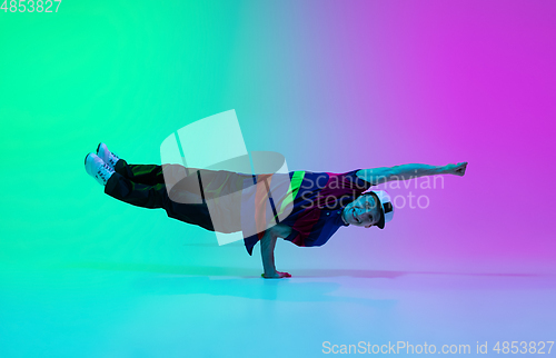 Image of Beautiful sportive boy dancing hip-hop in stylish clothes on colorful gradient background at dance hall in neon light.