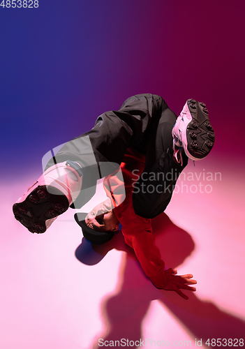 Image of Beautiful sportive boy dancing hip-hop in stylish clothes on colorful gradient background at dance hall in neon light.