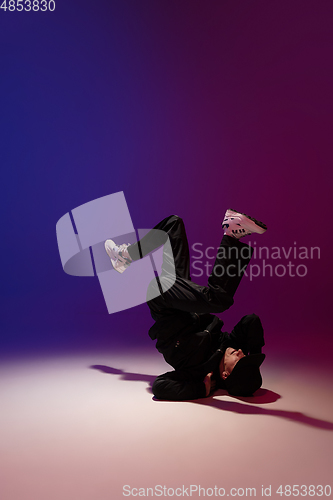 Image of Beautiful sportive boy dancing hip-hop in stylish clothes on colorful gradient background at dance hall in neon light.