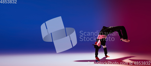 Image of Beautiful sportive boy dancing hip-hop in stylish clothes on colorful gradient background at dance hall in neon light.