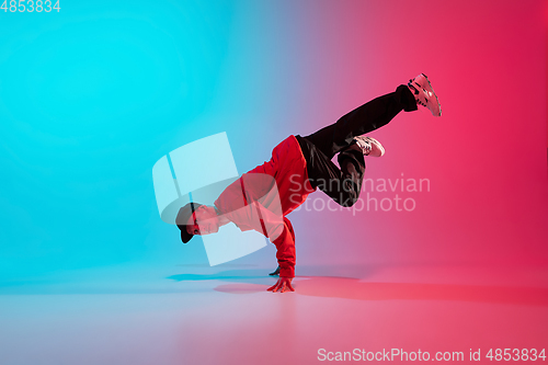 Image of Beautiful sportive boy dancing hip-hop in stylish clothes on colorful gradient background at dance hall in neon light.