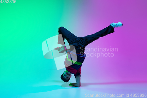 Image of Beautiful sportive boy dancing hip-hop in stylish clothes on colorful gradient background at dance hall in neon light.