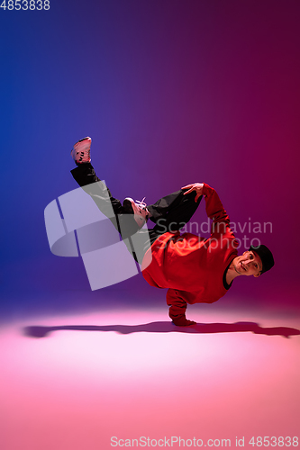 Image of Beautiful sportive boy dancing hip-hop in stylish clothes on colorful gradient background at dance hall in neon light.