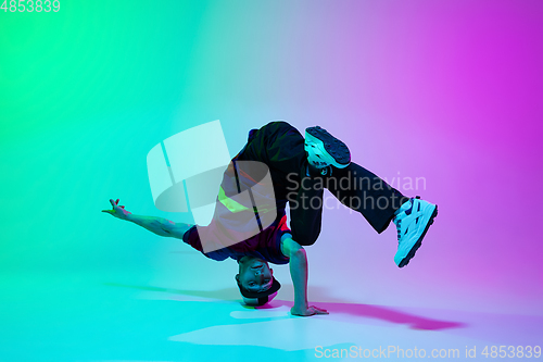 Image of Beautiful sportive boy dancing hip-hop in stylish clothes on colorful gradient background at dance hall in neon light.