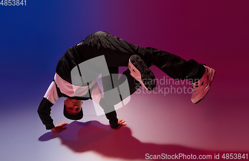 Image of Beautiful sportive boy dancing hip-hop in stylish clothes on colorful gradient background at dance hall in neon light.