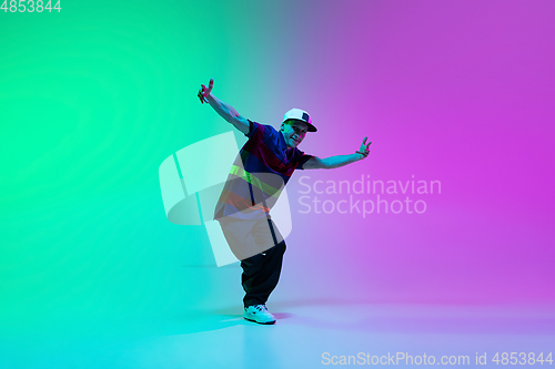 Image of Beautiful sportive boy dancing hip-hop in stylish clothes on colorful gradient background at dance hall in neon light.