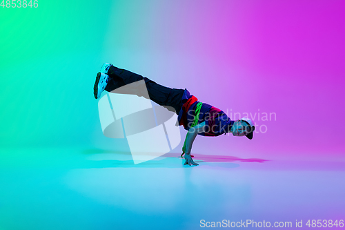 Image of Beautiful sportive boy dancing hip-hop in stylish clothes on colorful gradient background at dance hall in neon light.