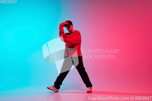 Image of Beautiful sportive boy dancing hip-hop in stylish clothes on colorful gradient background at dance hall in neon light.