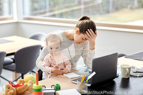 Image of tired mother with baby working at home office