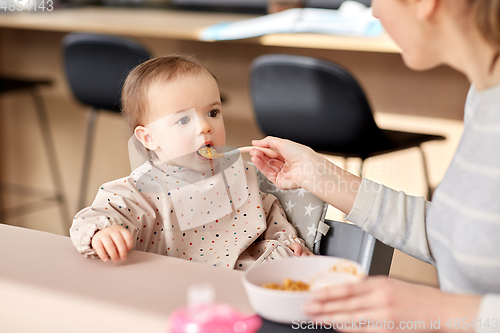 Image of happy mother feeding baby with puree at home