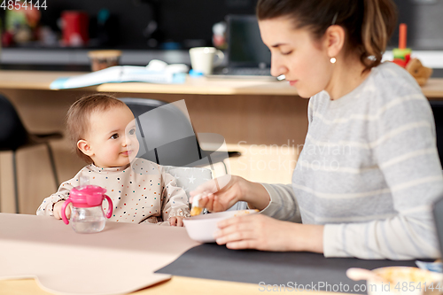 Image of happy mother feeding baby with puree at home