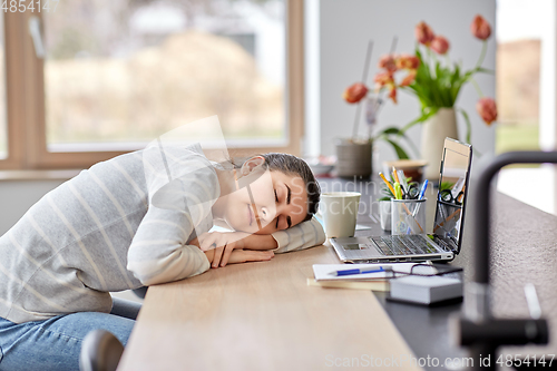 Image of tired woman sleeping on table with laptop at home