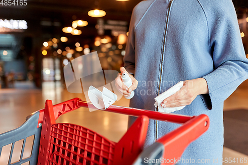 Image of woman cleaning shopping cart handle with sanitizer