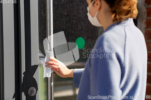 Image of woman in mask cleaning door handle with wet wipe