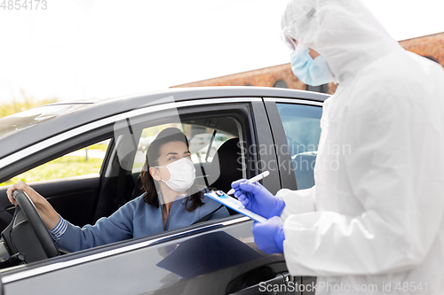 Image of healthcare worker with clipboard and woman in car