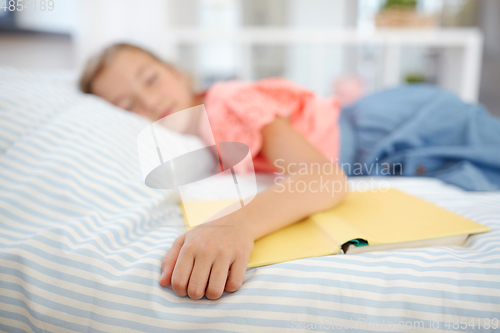 Image of little girl with book sleeping in bed at home